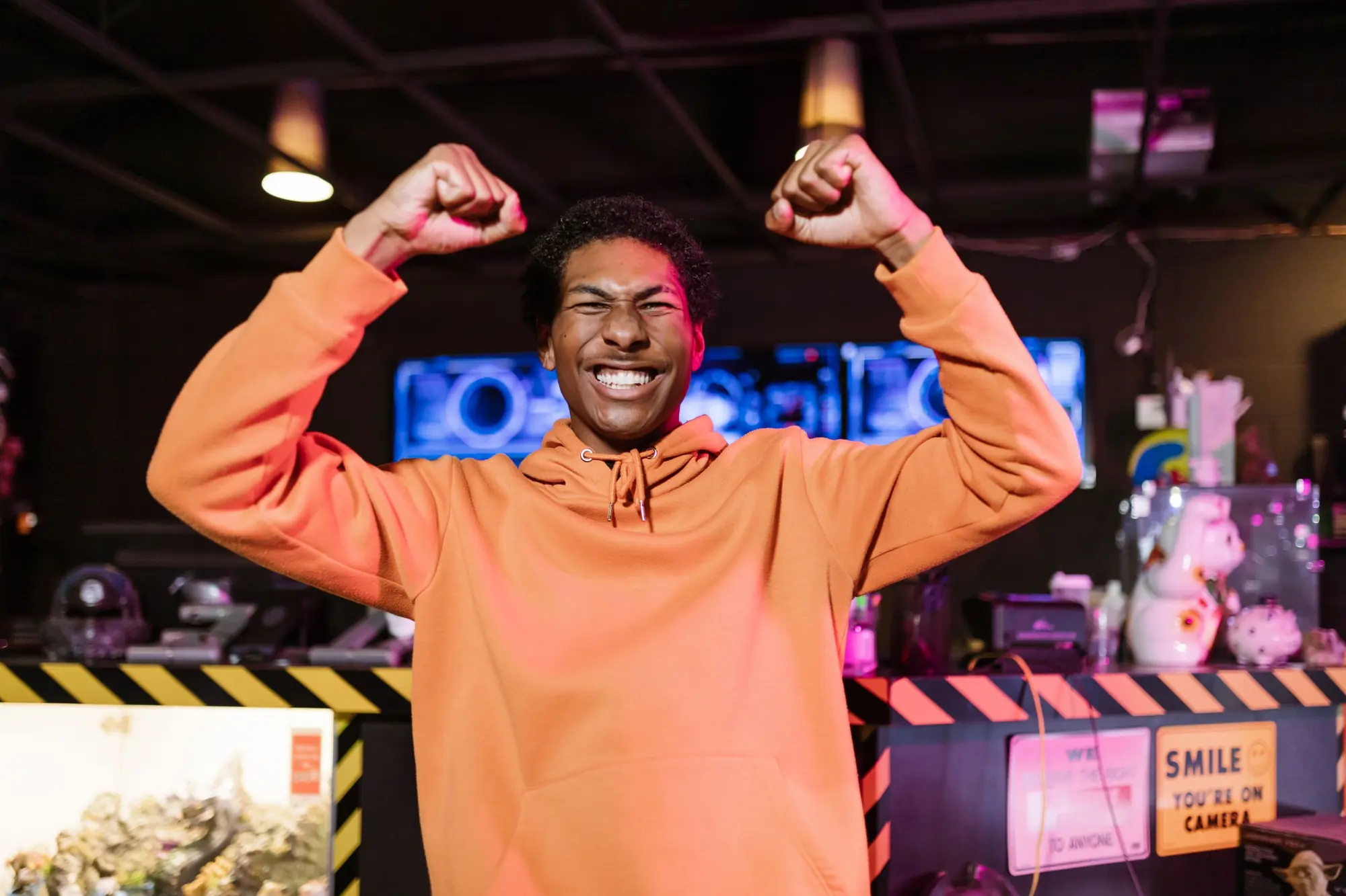 A young gamer throwing both fists up after winning, inside a gaming lounge